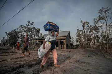 BERGEGAS LARI: Seorang wanita menyelamatkan barangannya berikutan letusan Gunung Semeru di kampung Kajar Kuning di Lumajang, Indonesia semalam. - Foto AFP