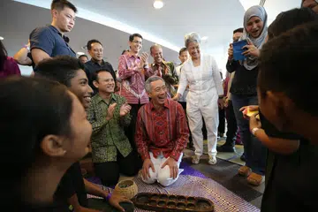Perdana Menteri, Encik Lee Hsien Loong (tengah), menyertai permainan congkak bersama pelajar Sekolah Menengah Orchid Park pada 2015, sebahagian acara di pelancaran Bulan Bahasa Melayu pada tahun itu. Bersamanya ialah isterinya, Cik Ho Ching (berdiri, baju putih), dan penjawat politik Melayu seperti Encik Masagos Zulkifli Masagos Mohamad (berdiri, tiga dari kanan),  Profesor Madya Dr Muhammad Faishal Ibrahim (berdiri, empat dari kanan); dan Encik Zaqy Mohamad (di sebelah Encik Lee).
