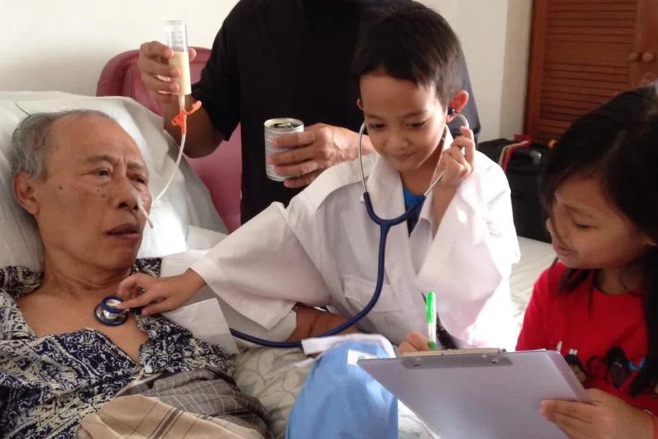 Terbaring di katil selepas diserang penyakit angin ahmar pada 2014, bapa Cik Nurhani (kiri) dijaga rapi dengan penuh kasih sayang oleh keluarga Cik Nurhani termasuk anak-anak kecilnya yang akan berlagak menjadi ‘doktor’ di sisi arwah bapanya. 
