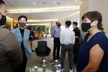 SEKATAN DILONGGARKAN: Menurut Cik Josephine Teo (dua dari kiri) sekatan kembali bekerja akan dilonggarkan menyusuli pengumuman pemerintah bahawa negara akan melangkah ke fasa ketiga hujung bulan ini. Beliau dan Menteri Kanan, Encik Tharman Shanmugaratnam (di belakang), telah melawat Singtel semalam. - Foto LIANHE ZAOBAO 