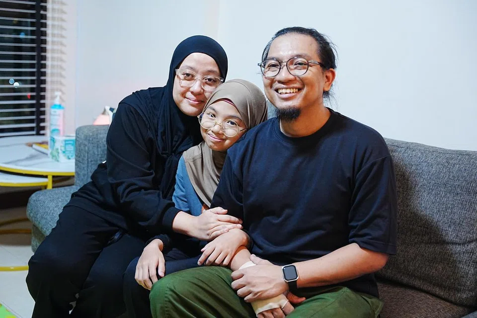 Ria Nadira Muhamad Rizal (tengah) bersama ayahnya, Encik Muhamad Rizal Monin (kanan), dan ibu tirinya, Cik Sofieyani Abdul Razak (kiri), di rumahnya di Fernvale Road. 