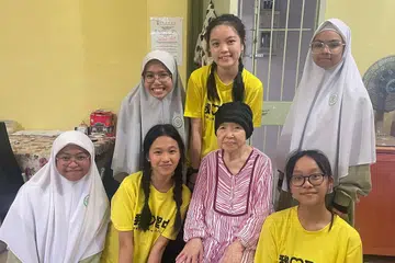 Pelajar MAI (bertudung) dan murid Sekolah Tinggi Anglican (AHS) menziarahi penerima habuan baucar (tengah, baju belang merah) dan barangan runcit di Lorong 7 Toa Payoh, pada April 2023.