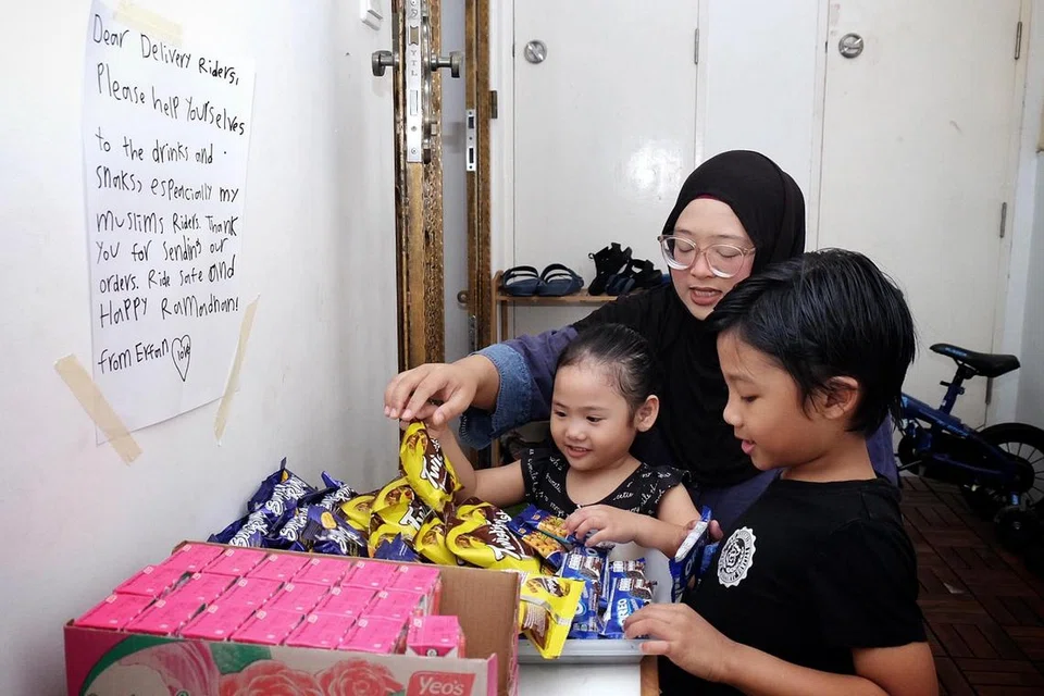 KONGSI REZEKI: Cik Erma Othman, 33 tahun, bersama dua anaknya, Erfan M. Ridzwan (kanan) dan Enya M. Ridzwan (kiri), menyediakan minuman kotak serta makanan ringan di luar rumah mereka bagi pekerja penghantaran makanan untuk berbuka puasa ketika bekerja. - Foto BM oleh KHALID BABA