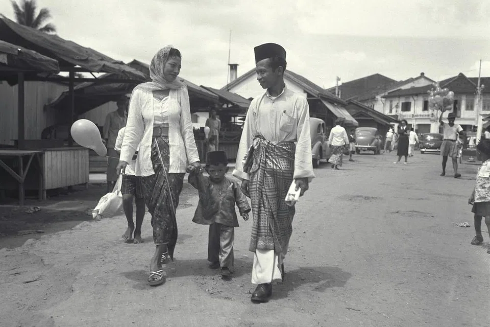 Encik Suhaimi Samian (kanan) bersama isteri dan anaknya pulang ke rumah mereka di kawasan Geylang Serai selepas pergi kunjung-mengunjung pada Hari Raya. Gambar ini diambil sekitar tahun 60-an. 