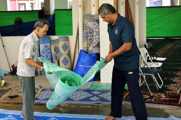BERAT SAMA DIPIKUL: Encik Yusoff Subri (baju biru) dan seorang lagi relawan membentang tikar dan sejadah sebelum jemaah menunaikan solat tarawih di kolong Blok 724 Jurong West Street 72. - Foto KHALID BABA 