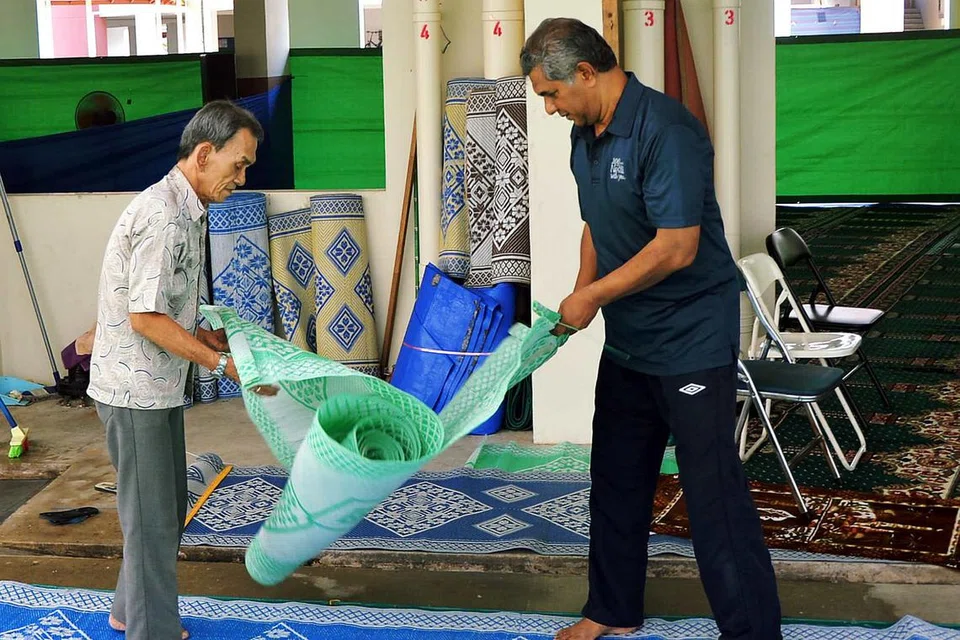 BERAT SAMA DIPIKUL: Encik Yusoff Subri (baju biru) dan seorang lagi relawan membentang tikar dan sejadah sebelum jemaah menunaikan solat tarawih di kolong Blok 724 Jurong West Street 72. - Foto KHALID BABA 