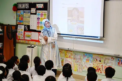 Cik Salamah menggunakan mikrofon untuk mengajar dalam kelasnya.