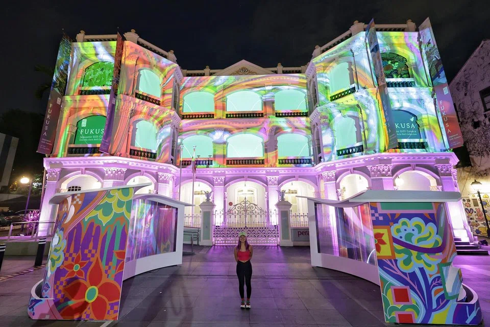 Artis filem, Clare Chong, berdiri di depan persembahan seni pemasangan dan paparan cahaya, ‘Between Threads’, di Muzium Peranakan, sebagai sebahagian Pesta Malam Singapura 2024.