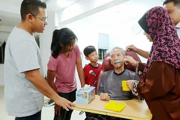 PERLU SOKONGAN TIDAK BERBELAH BAHAGI DARIPADA KELUARGA: Cik Zaharah Roosdi (kanan) sedang membantu suaminya, Encik Hurairah Padilah, minum air dengan menggunakan sudu sambil disaksikan anak mereka, Encik Zaki (kiri) dan dua cucu mereka. - Foto BM oleh SAINI SALLEH