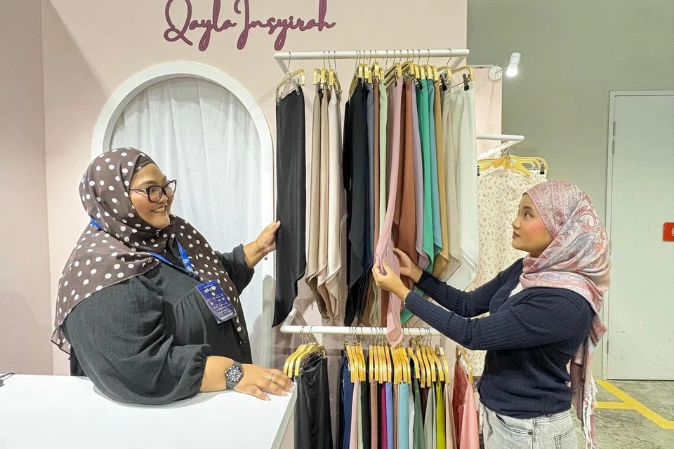 Penyelia Qayla Insyirah, Cik Jannah Isa (kiri), melayani pelanggan, Cik Efi Batrisyia Rio Noramin, 22 tahun, di reruai Qayla Insyirah – jenama tudung dalam talian – di Absolut Bazaar Gaya Raya di Kuala Lumpur.