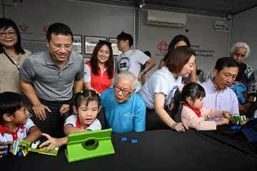 Menteri Kesihatan, Encik Ong Ye Kung (duduk, kanan) melakukan kegiatan robotik bersama pelajar tadika. Beliau ditemani Menteri Pembangunan Negara, Encik Desmond Lee (berbaju polo kelabu) dalam majlis pelancaran Hab Penduduk Kita di West Coast pada 2 April.