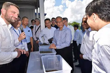 PANDANG KE HADAPAN: Encik Masagos (memegang bekas plastik) mendengar taklimat seorang pegawai berkenaan proses mengubah sisa menjadi sumber berguna. - Foto CMG