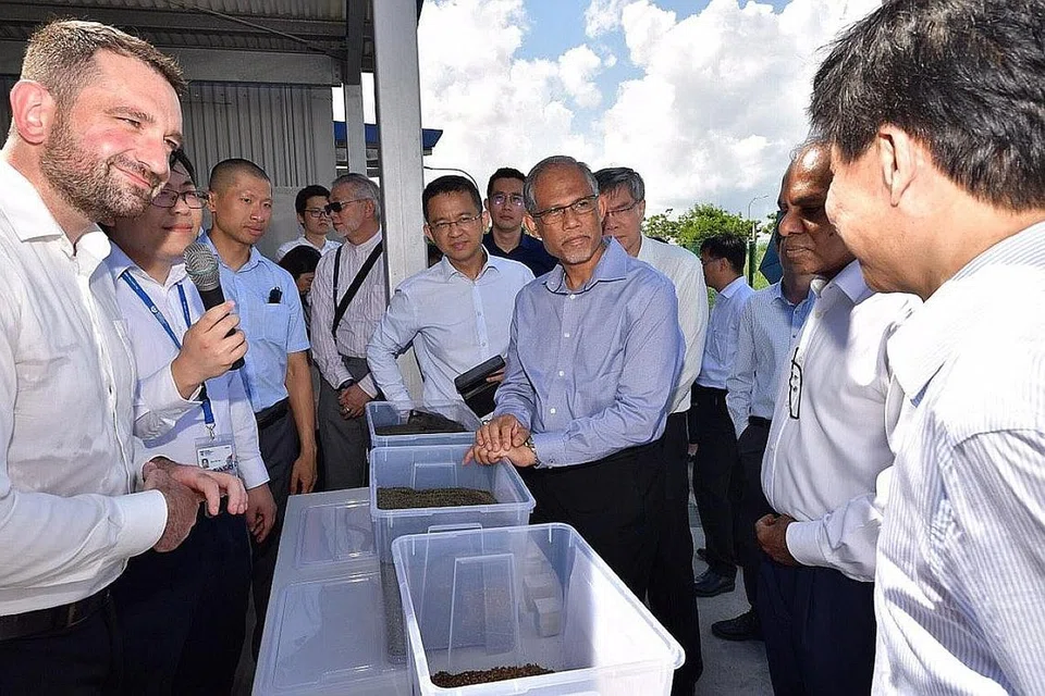 PANDANG KE HADAPAN: Encik Masagos (memegang bekas plastik) mendengar taklimat seorang pegawai berkenaan proses mengubah sisa menjadi sumber berguna. - Foto CMG