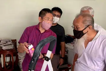 UBAH KEPADA BAL LAMPU PENJIMAT TENAGA: Dr Mohamad Maliki Osman (kiri) sedang menjelaskan kepada penduduk yang dikenali sebagai Encik Yeo tentang penggunaan bal lampu penjimat tenaga bagi mengurangkan kos bil elektrik. - Foto PEJABAT KAWASAN UNDI SIGLAP