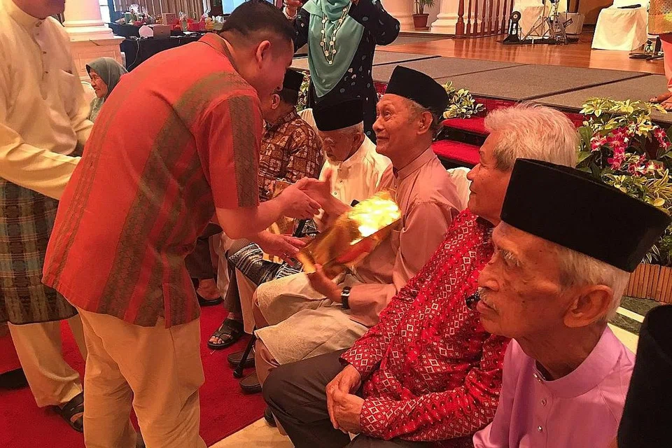 BUAL MESRA: Encik Amrin (membongkok, di kiri sekali) berbual sambil menyampaikan cenderahati kepada antara warga perintis Bussorah Street, Encik Mohd Salleh Haji Abdul Tain.