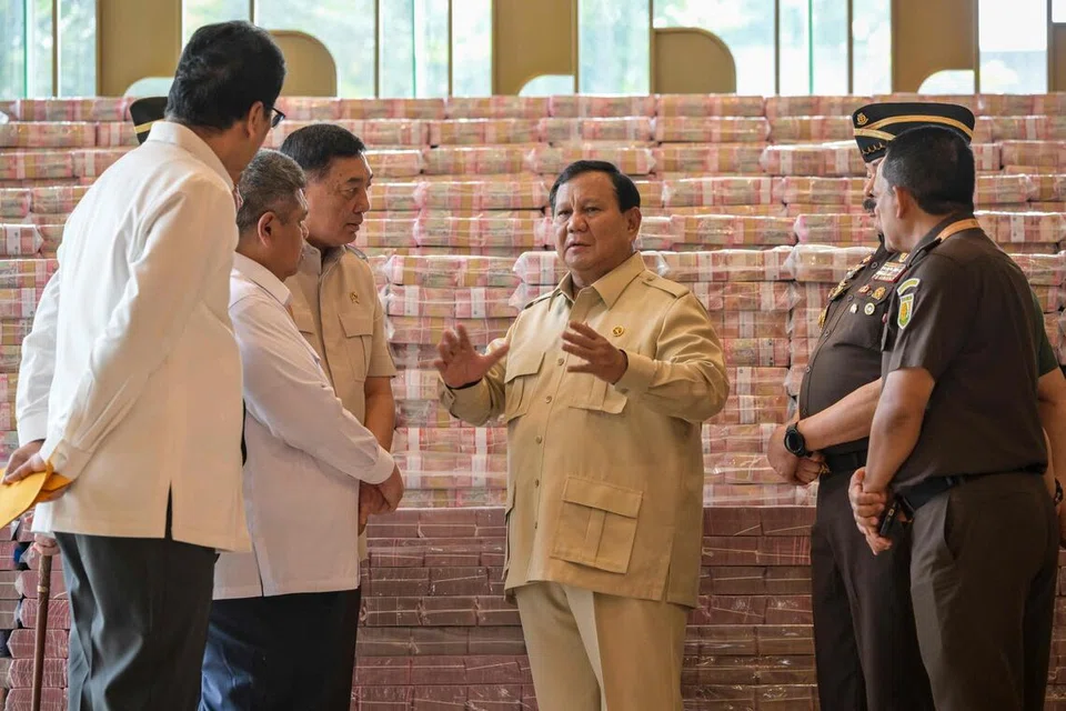 Presiden Indonesia Prabowo Subianto (tengah), berbincang dengan beberapa pegawai kanan termasuk Peguam Negara Sanitiar Burhanuddin (dua dari kanan); Menteri Pertahanan Sjafrie Sjamsoeddin (tiga dari kiri) dan Menteri Kewangan Purbaya Yudhi Sadewa (kiri), di sisi longgokan wang kertas rupiah Indonesia bernilai bersamaan lebih AS$800 juta ($1.04 bilion) di bangunan Pejabat Peguam Negara, semasa majlis penyerahan aset daripada kes rasuah kemudahan eksport minyak sawit mentah (CPO) di Jakarta pada 20 Oktober.