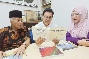 JERIH PERIH JEJAK BEKAS PENGHUNI PONDOK BAWEAN BERBALOI: Tiga orang kuat Persatuan Bawean Singapura - presiden Encik Faizal Wahyuni (tengah), penasihat Encik Mohd Seain Matsom dan penolong setiausaha Cik Nurul Sa'adah Mohd Seain - meneliti buku 'Ponthuk Bawean di Singapura'. - Foto BH oleh SAINI SALLEH