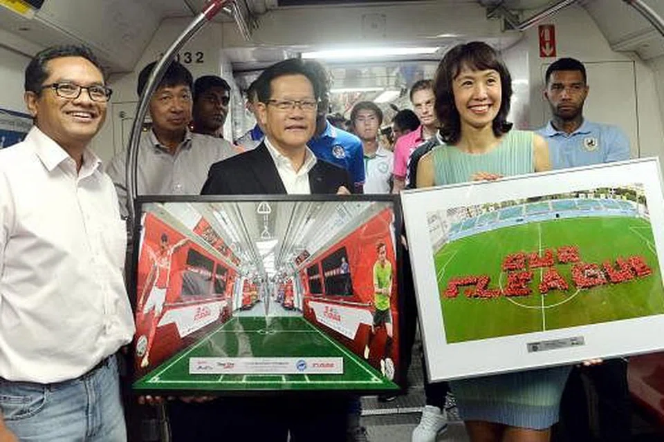 KERETA API LIGA-S: Encik Lim (berjaket hitam) dan Cik Low saling bertukar momento dalam perkongsian terbaru di antara SMRT dan FAS. Turut hadir adalah Presiden FAS, Encik Zainudin Nordin (kiri).