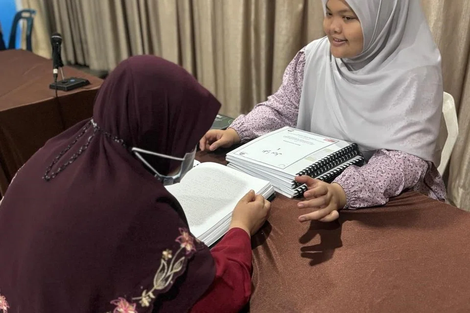 Ustazah Siti Nur Qurratu’ain Mohamad Noh (kanan) mengajar seorang pelajar cacat penglihatan membaca Al-Quran Braille.