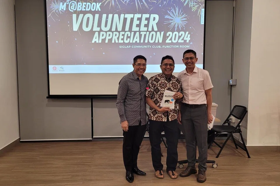 Dr Maliki (kiri) dan Encik Raihan (kanan) menyampaikan saguhati berbentuk buku kepada sukarelawan, Encik Azri Zulfarhan Kamsin.