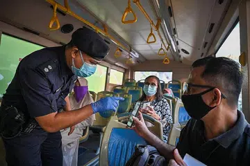 SEDIA DIPERIKSA: Seorang anggota polis memeriksa dokumen seorang penumpang semasa bas berhenti di sekatan polis di Kuala Lumpur di tengah-tengah pelaksanaan perintah sekatan pergerakan penuh di seluruh negara yang berkuat kuasa semalam dan berlangsung sehingga 14 Jun ini. - Foto AFP 