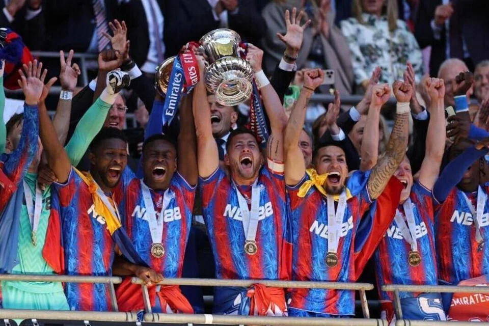 Pemain Pertahanan Crystal Palace, Marc Guehi (tiga dari kiri) dan Joel Ward (empat dari kiri) menjulang trofi ketika pemain Crystal Palace meraikan kemenangan selepas final Piala FA menentang Manchester City di Stadium Wembley, London, pada 17 Mei 2025. Palace menewaskan Manchester City 1-0 untuk memenangi trofi utama pertama dalam sejarah kelab.