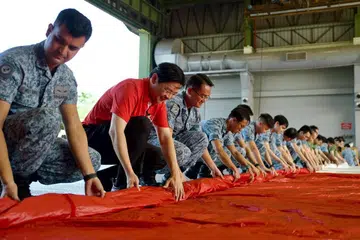 BUAT PERSIAPAN: Timbalan Perdana Menteri, Encik Lawrence Wong (dua dari kiri), melawat Pangkalan Udara Sembawang pada 5 Julai untuk menolong melipat bendera negara yang akan dikibarkan pada Perbarisan Hari Kebangsaan 2023.