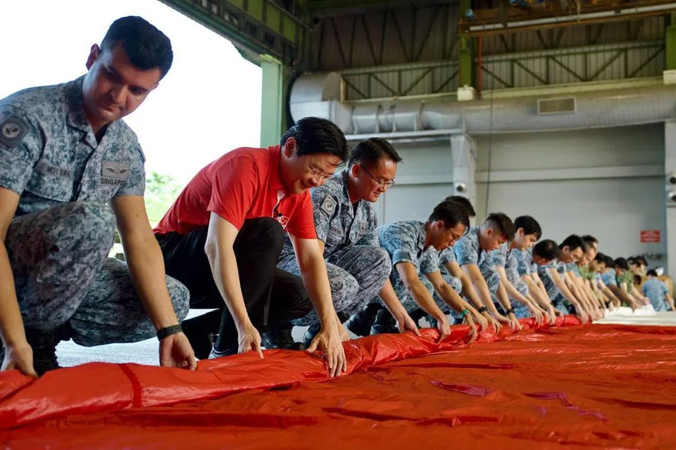 BUAT PERSIAPAN: Timbalan Perdana Menteri, Encik Lawrence Wong (dua dari kiri), melawat Pangkalan Udara Sembawang pada 5 Julai untuk menolong melipat bendera negara yang akan dikibarkan pada Perbarisan Hari Kebangsaan 2023.