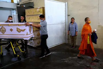 TRAGEDI MENYAYAT HATI: Seorang sami Buddha dan pegawai polis membawa keranda yang mengandungi mayat seorang mangsa dari Myanmar di Institut Sains Forensik Bangkok dalam. Warga Myanmar ini adalah antara dua mangsa yang terbunuh dalam insiden tembakan di pusat beli-belah Siam Paragon pada Selasa.