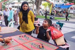 Seorang kanak-kanak bermain permainan tradisional Melayu dipanggil, batu seremban, buat kali pertama sambil diperhatikan ibunya.