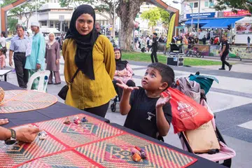 Seorang kanak-kanak bermain permainan tradisional Melayu dipanggil, batu seremban, buat kali pertama sambil diperhatikan ibunya.