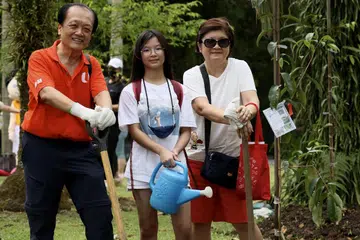 TANAM POKOK: Encik Leong Chun Chong (paling kiri) bersama cucunya Celyn Sim (tengah) dan isterinya Lily (kanan), bersebelahan pokok Derum Bukit yang mereka tanam di Taman Pasir Ris pada Sabtu.