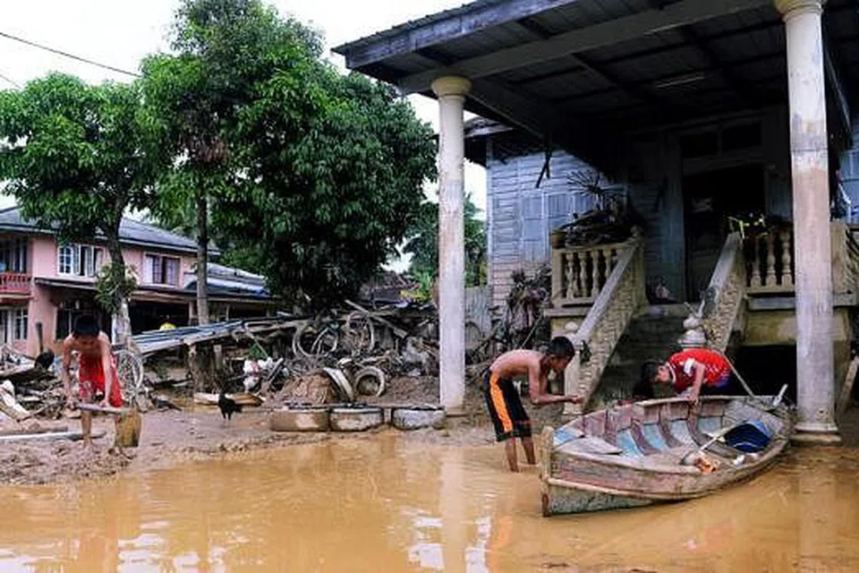 BANJIR KEMBALI SURUT: Kanak-kanak ini mencuci sampan di depan rumah mereka dengan menggunakan air banjir yang semakin surut.