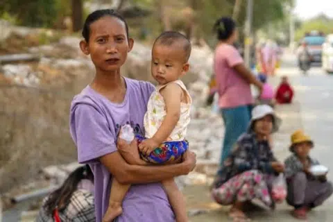 Seorang ibu yang menggendong anaknya dan beberapa yang lain sedang menunggu bantuan kemanusiaan di Sagaing, Myanmar, pada 2 April.
