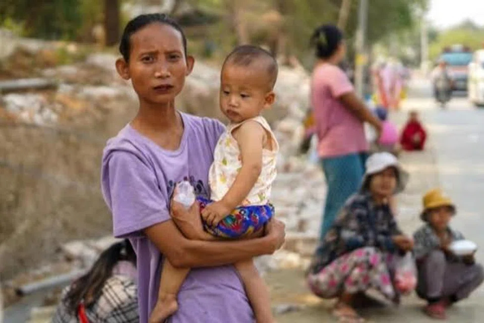 Seorang ibu yang menggendong anaknya dan beberapa yang lain sedang menunggu bantuan kemanusiaan di Sagaing, Myanmar, pada 2 April.