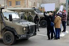 Aktivis Palestin dan Israel memegang sepanduk di hadapan pasukan keselamatan serta kenderaan tentera Israel semasa bantahan menentang rang undang-undang Israel yang mengusulkan hukuman mati mandatori terhadap militan Palestin yang disabit membunuh rakyat Israel, berhampiran Beit Jala di Tebing Barat yang diduduki Israel, 19 Disember 2025. 