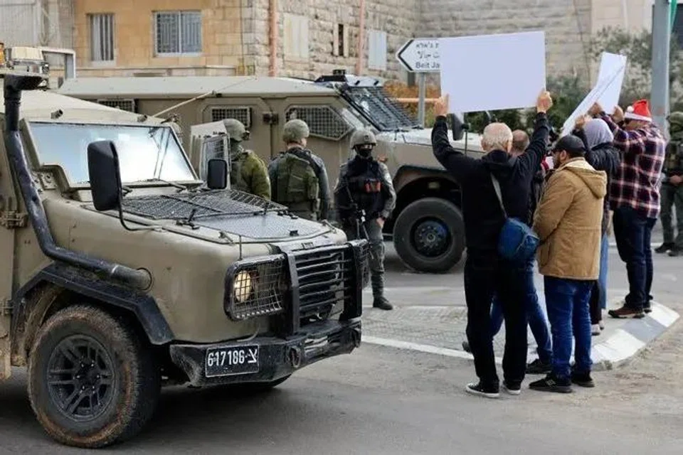 Aktivis Palestin dan Israel memegang sepanduk di hadapan pasukan keselamatan serta kenderaan tentera Israel semasa bantahan menentang rang undang-undang Israel yang mengusulkan hukuman mati mandatori terhadap militan Palestin yang disabit membunuh rakyat Israel, berhampiran Beit Jala di Tebing Barat yang diduduki Israel, 19 Disember 2025. 