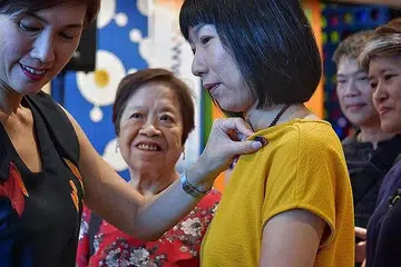 IKTIRAF SUMBANGAN ISTERI DAN IBU ANGGOTA NS: Cik Teo (kiri) meletakkan pin kolar di blaus suri rumah, Cik Jenny Sim, semasa di acara pelancaran inisiatif 'Everyday (Her)oes' semalam. - Foto BH oleh NG SOR LUAN