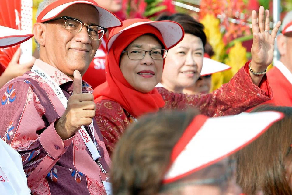 TONTON NDP BERSAMA: Mantan Speaker Parlimen, Cik Halimah Yacob, bersama suaminya, Encik Mohammed Abdullah Alhabshee, yang menunjukkan tanda jempol, menyambut Hari Kebangsaan dengan menonton NDP bersama sekitar 25,000 penonton di Pentas Terapung Marina Bay.
