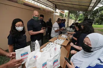 SAMA-SAMA MEMBANTU: Sukarelawan daripada Kedutaan Amerika Syarikat ke Singapura, Cik Jenny Kim (kiri) dan Encik Daniel Caporaso sedang membungkus pek yang akan diagihkan bersama para sukarelawan daripada Masjid Mujahiddin dan Kuil Sri Muneeswaran. - Foto BH oleh KELVIN CHNG