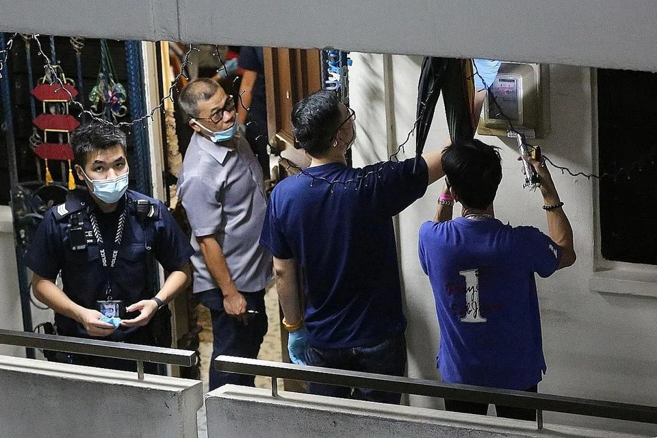 BUAT PEMERIKSAAN: Polis mengawal sedang beberapa orang dilihat memeriksa peti litar elektrik di luar rumah pasangan suami isteri yang meninggal di Blok 120 Ho Ching Road. - Foto SHIN MIN