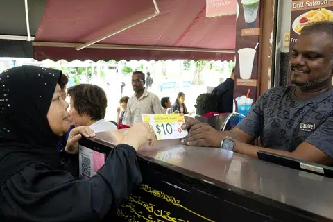Seorang penerima manfaat, Cik Faridah Salamat (kiri), 65 tahun, menebus baucar makan bernilai $10 di kedai makan Mohamed Waseef. Bersamanya ialah pemilik kedai makan Mohamed Waseef, Encik Sathik Ali (kanan).