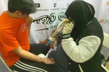 Cik Tessa Abigail (kanan) mengacukan sinar laser ke lengan Encik Andi Darmawan yang bertatu, sebagai prosedur membuang tatu di bazar Raya di Jakarta. 