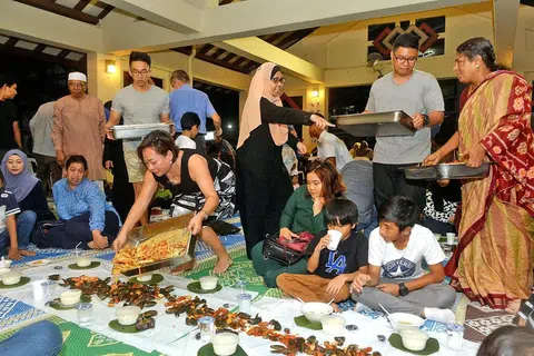 'KENDURI' MAKANAN LAUT: Cik Noreeni (bertudung di tengah) menganjurkan sesi iftar 'shell-out' bagi merapatkan hubungan bersama keluarga, jiran dan teman termasuk yang bukan beragama Islam. - Foto KHALID BABA