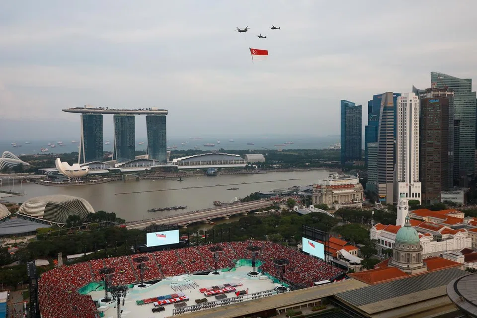 TERBANG LALU BENDERA: Bendera Singapura yang dibawa  helikopter Chinook terbang lalu di Perbarisan Hari Kebangsaan di Padang,  diiringi dua helikopter Apache.