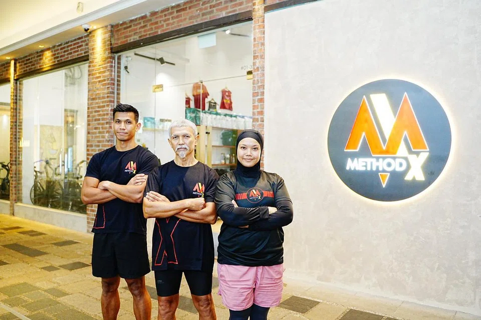 Dua adik-beradik itu, Encik Hafiz (kiri) dan Cik Norliyana (kanan) telah membuka gimnasium kecergasan di Gopeng Street sejak 2023. Bapanya, Encik Jumahat (tengah) berasa bangga dengan pencapaian anaknya ini.