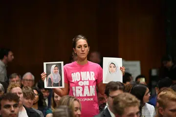 Seorang penunjuk perasaan antiperang mengangkat gambar ketika Setiausaha Pertahanan Amerika Syarikat, Pete Hegseth, memberi keterangan di hadapan Jawatankuasa Peruntukan Senat di Capitol Hill, Washington pada 21 Julai 2026. Hegseth memohon dana tambahan AS$87 bilion bagi membiayai operasi ketenteraan, termasuk perang yang semakin memuncak dengan Iran.