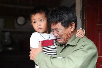 SEBAK KEHILANGAN ANAK: (Atas) Encik Le Minh Tuan, bapa kepada Cik Le Van Ha, yang dikhuatiri merupakan salah seorang mangsa, tidak dapat menahan tangisannya sambil mendukung anak Cik Ha di luar rumah mereka di wilayah Nghe An, Vietnam. - Foto AFP 