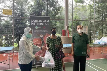 BANTU RINGAN BEBAN: Cik Meenachi (tengah) menerima habuan daging korban daripada Cik Rahayu (kiri) dan Encik Abdul Halim (kanan) di pengagihan daging korban Jamiyah di gelanggang bola keranjang berdekatan Blok 266 Bukit Batok East 4 semalam. - Foto BH oleh ZULAIQAH ABDUL RAHIM