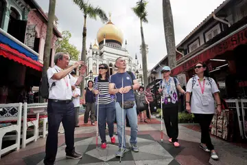 JALAN KENANGAN: Encik Chhua Bak Siang (kiri), 71 tahun, memimpin golongan cacat penglihatan dari Guide Dogs Singapore melawat sekitar Bussorah Street. - Foto BH oleh KELVIN CHNG
